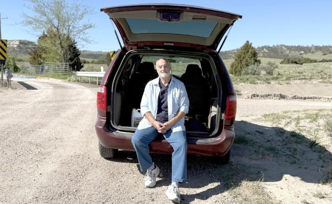 Roger McDonald sits in the back of his preferred rural mail delivery vehicle, a Dodge Caravan, on a gravel road along his 150-mile route outside Scottsbluff in northwestern Nebraska on May 11, 2025. The 61-year-old letter carrier worries about what would happen to his customers, his coworkers and himself if the Postal Service further curtailed service or was privatized. (Courtesy Photo: Nick Loomis/The Midwest Newsroom)